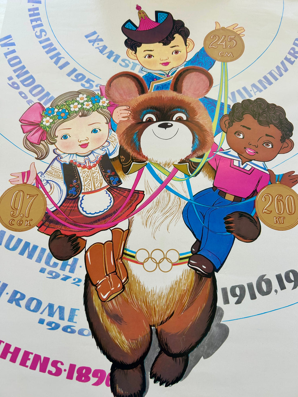 Illustration of a bear character with two children on a circular design with Olympic-themed text.