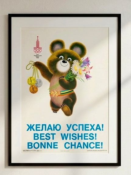 Framed Moscow Olympics poster with a cartoon bear holding flowers and Olympic rings, text in multiple languages.