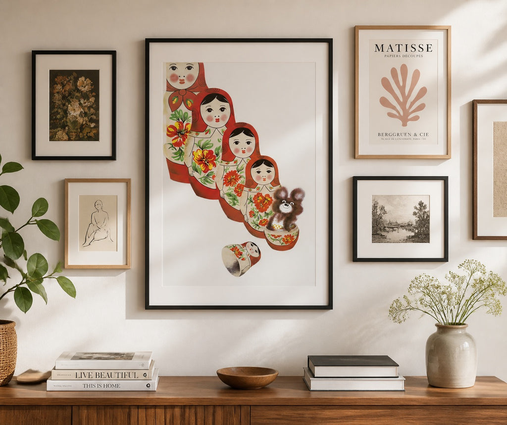 Wall with framed artwork including a colorful Russian doll print, a plant, and books on a wooden surface.