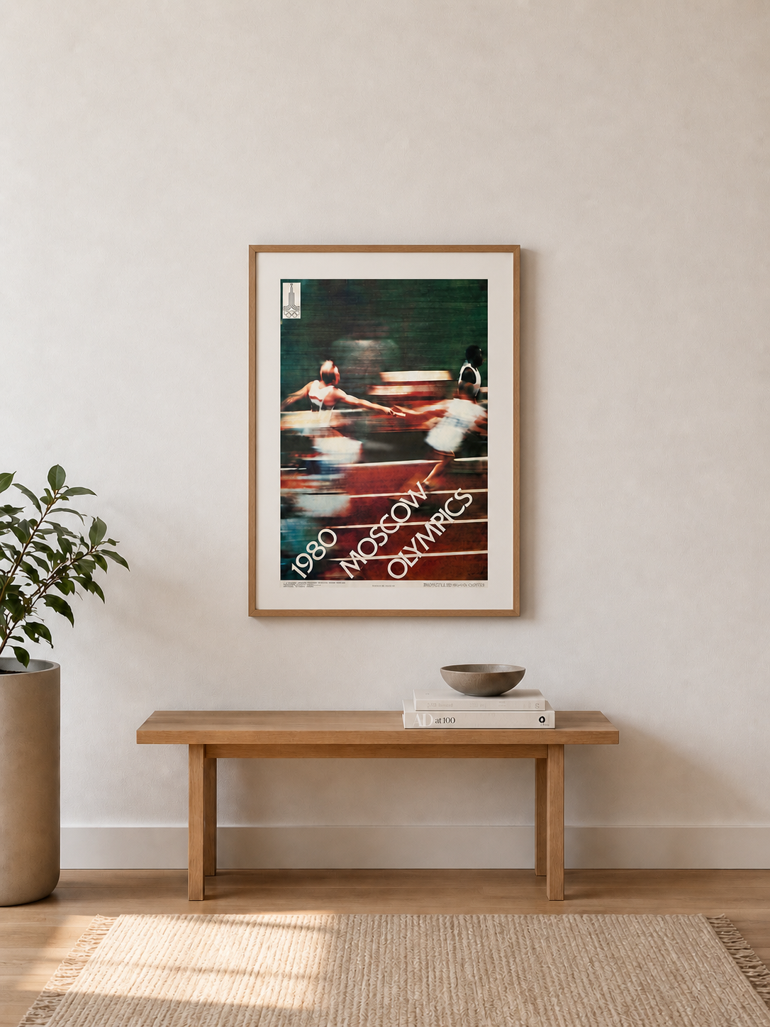 Framed artwork on a wall above a wooden bench in a room with a plant and books.