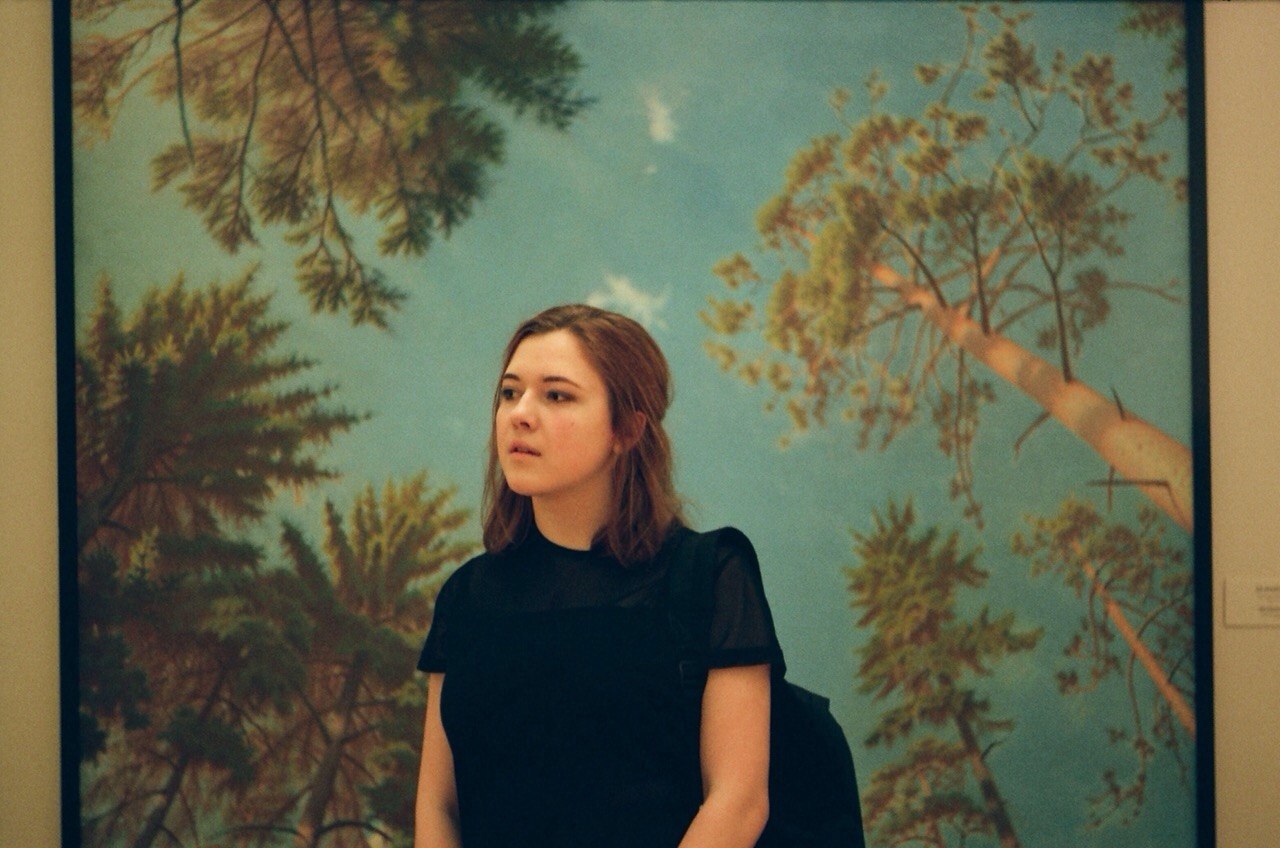 Woman sitting in front of a forest mural on a wall.